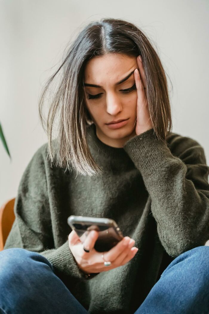 Young woman in green sweater looking worried while holding a smartphone, reflecting on middle class challenges for Gen Z.