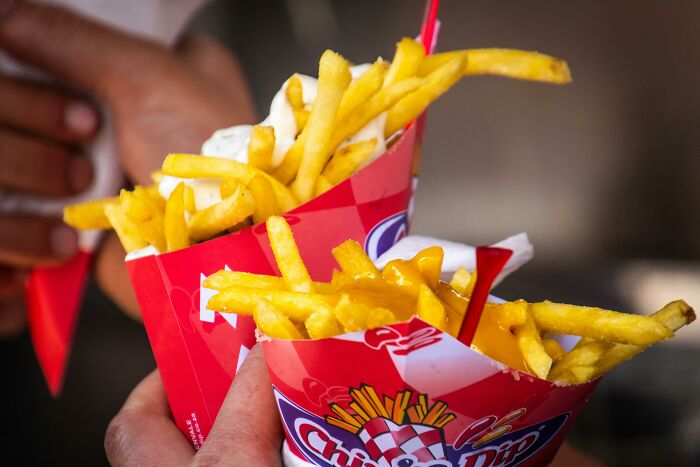 Two hands holding servings of cheesy and regular French fries, highlighting French fries and Diet Coke for migraine relief.