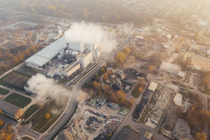 Aerial view of an industrial area with smoke rising from factory chimneys and roads winding through the site.