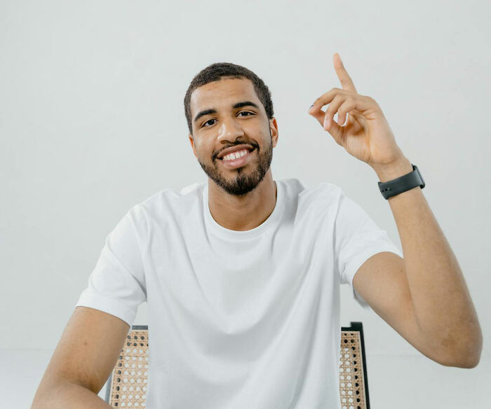 Smiling teacher in a white shirt raising a finger with confident expression, showing unhinged but effective teaching methods.