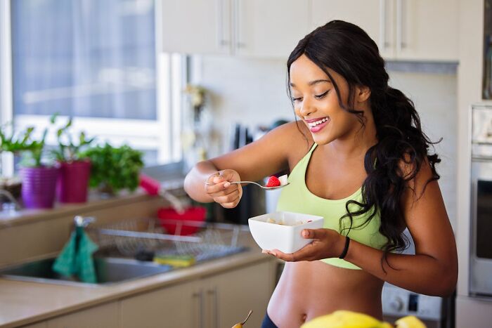 Young woman enjoying a healthy breakfast in kitchen, representing improved quality of life and positive lifestyle changes.