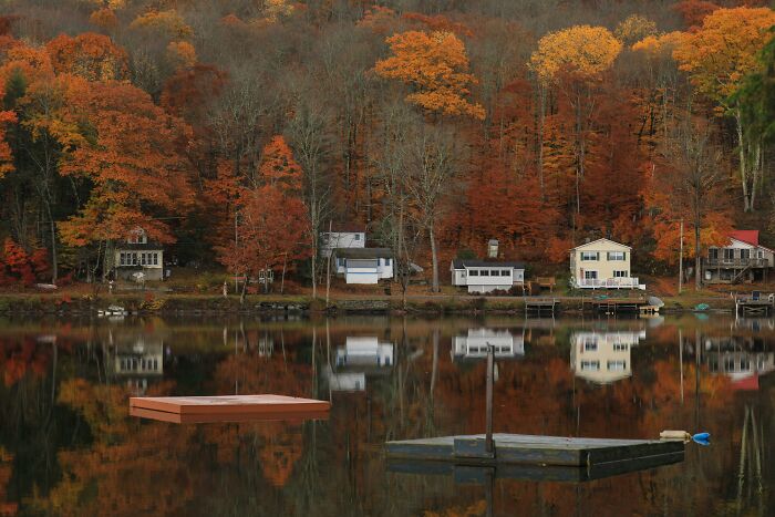 Calm lake reflecting colorful autumn trees and secluded houses at a tourist destination fallen into oblivion.