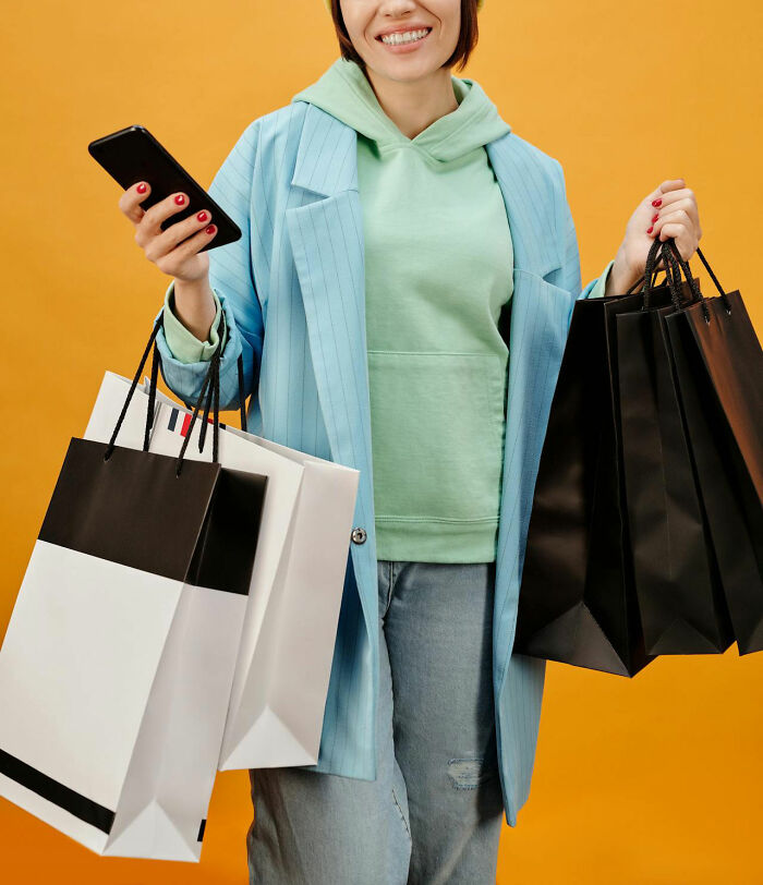 Young Gen Z woman holding multiple shopping bags and a smartphone, symbolizing middle class spending challenges.