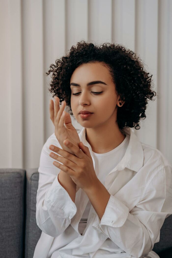 Young woman in a white shirt closing her eyes and gently holding her wrist, showing signs related to serotonin syndrome.