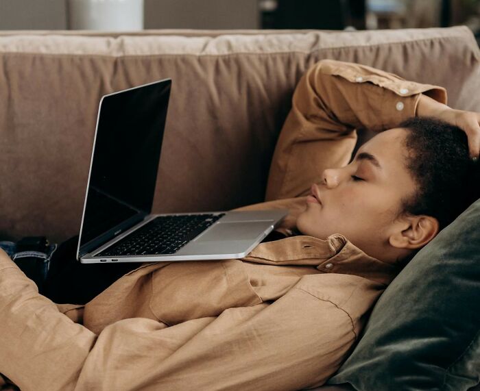 Person lying on a couch with a laptop balanced on their chest showing excessively lazy behavior at home.
