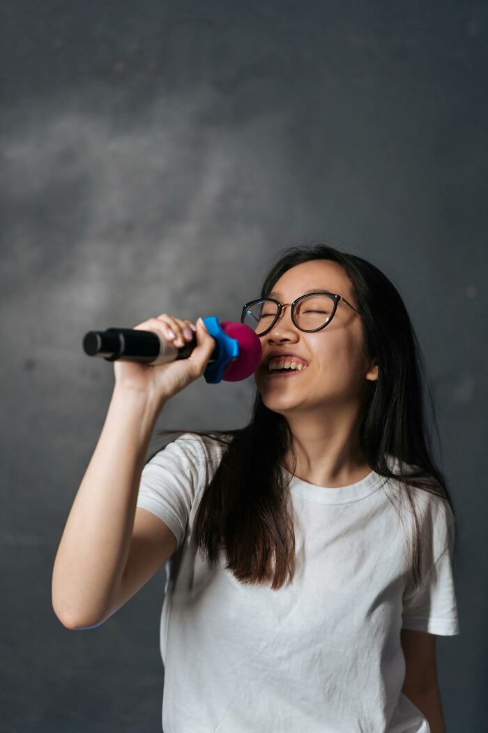 Young female teacher holding a microphone, smiling and engaging in unhinged but effective teaching methods.