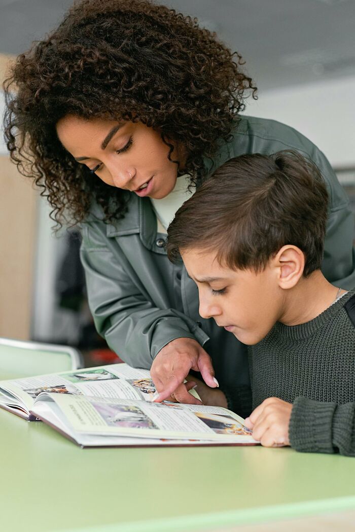 Woman teaching a young boy while pointing at a book, illustrating learning about serotonin syndrome symptoms and effects.