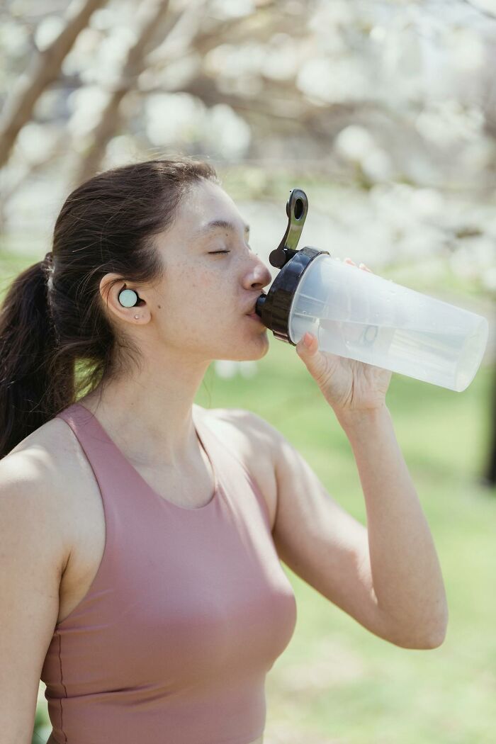Young woman drinking water from a shaker bottle outdoors, promoting health and awareness of serotonin syndrome symptoms.