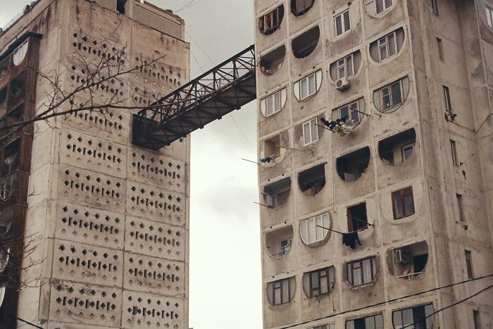 Aged concrete apartment buildings connected by a narrow metal bridge, illustrating urban life memories of Gen X.