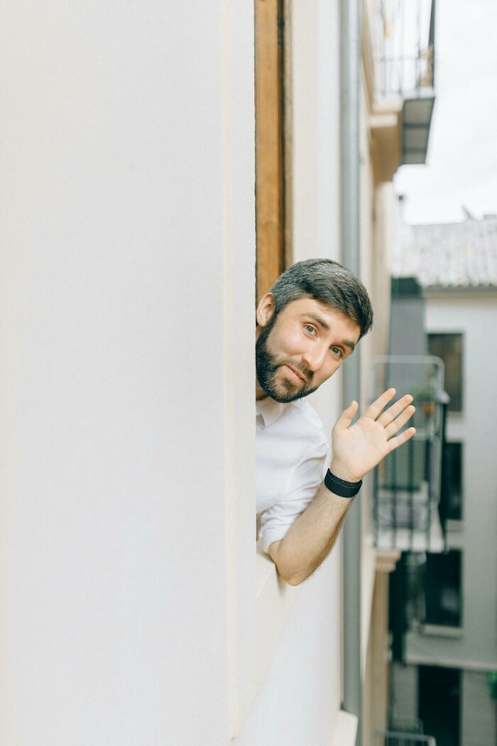 Man leaning out window waving hand with uncertain expression, illustrating moments women felt instantly unsafe with a man.