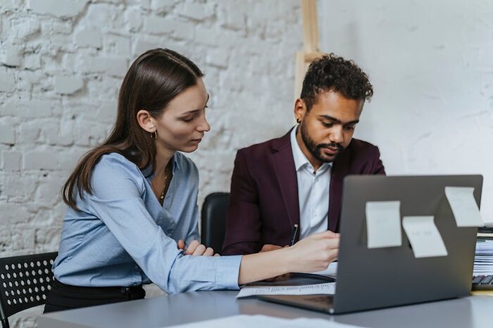 Two coworkers discussing documents and working on a laptop highlighting jobs earning concerns in office setting