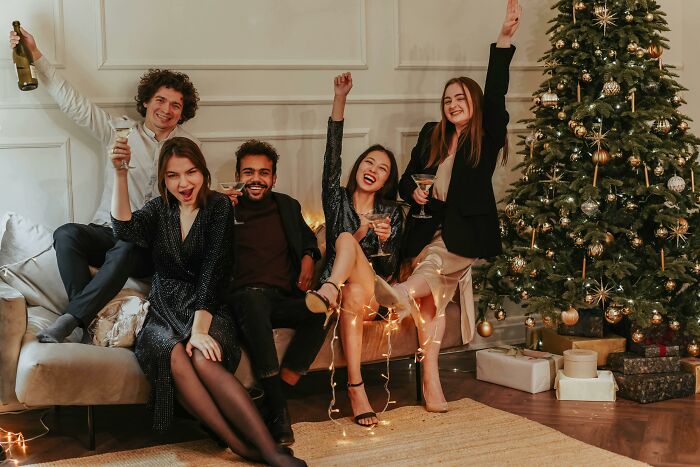 A group of adults celebrating by a Christmas tree, capturing moments that feel like being picked last in gym class again.