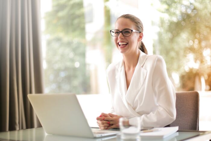 Businesswoman smiling at a laptop during a meeting, illustrating jobs that shouldn’t be earning as much as they do.