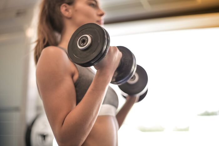 Woman lifting dumbbells in a gym using real-life cheat codes for effective and consistent workout results.