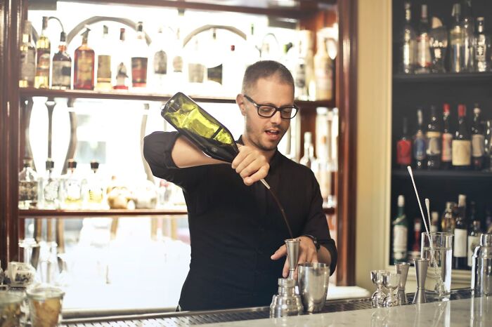 Bartender pouring a drink behind the bar, revealing industry secrets in a lively, well-stocked setting.