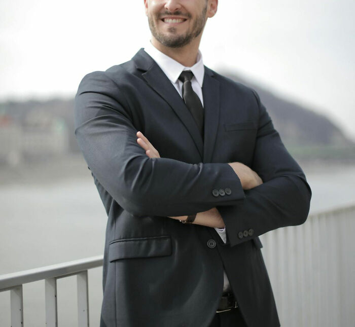Man in a dark suit and tie standing with arms crossed outdoors, representing questions women would ask men.