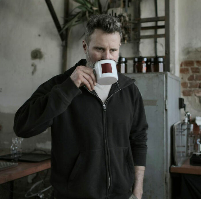 Man in a black zip-up jacket drinking coffee in an industrial setting, reflecting on unhinged but effective teacher strategies.