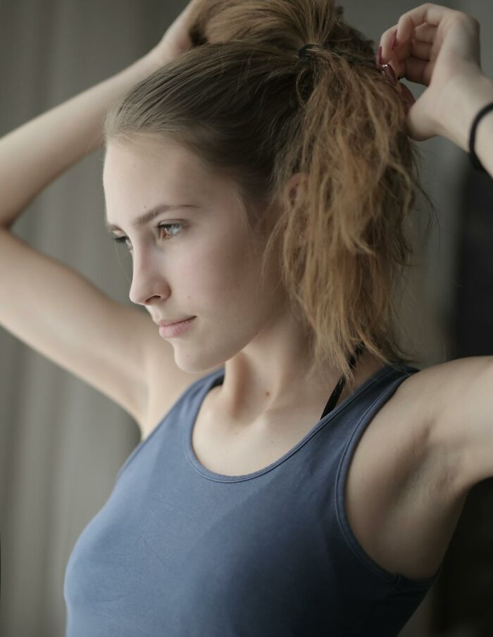 Young woman in a sleeveless top tying her hair, reflecting on questions women would ask men without judgment.