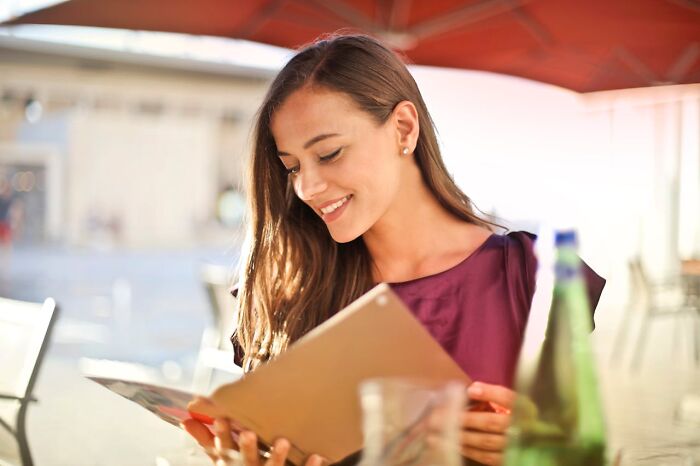 Young woman smiling and reading a menu outdoors, illustrating common boomer opinions people actually agree with.