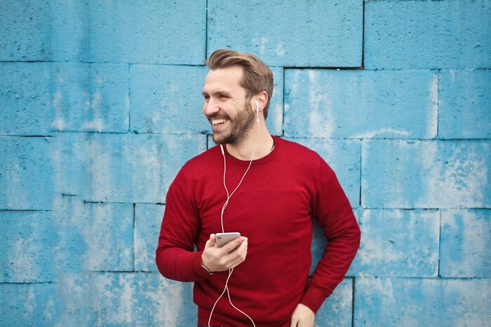 Man in a red sweater smiling and listening to music with earphones against a textured blue wall representing quality of life improvement.