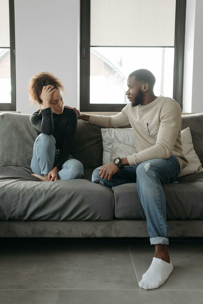 Woman looking distressed while a man gently touches her shoulder on a couch, highlighting feeling instantly unsafe with a man.