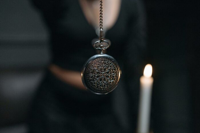 A person holding a vintage pocket watch on a chain near a lit candle in a dark setting representing weird ways to earn money.