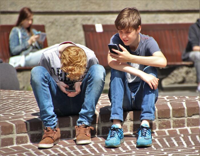 Two teenage boys sitting outdoors on brick steps, focused on their smartphones, illustrating middle class and Gen Z.