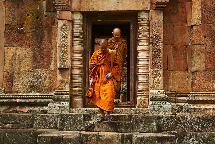 Two Buddhist monks in orange robes walking down stone steps of an ancient temple, illustrating cultural differences.