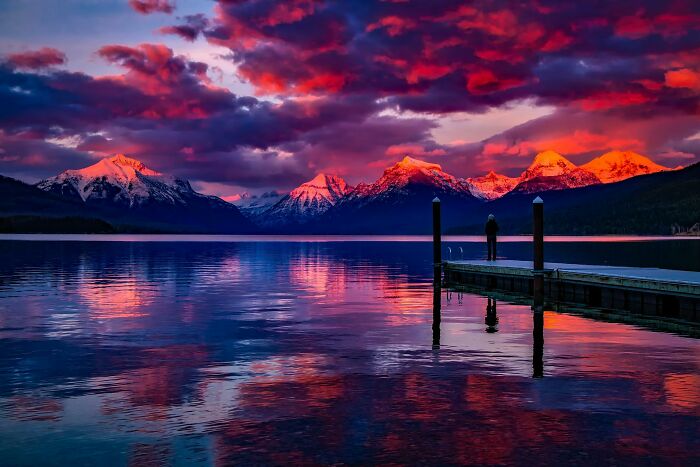 Person standing on a dock at sunset, enjoying low-key pleasures with vibrant mountain and lake reflections.