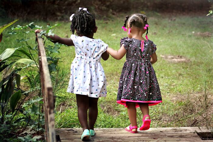 Two young girls holding hands and walking outdoors on a wooden path, symbolizing friendship and support after calling off wedding.