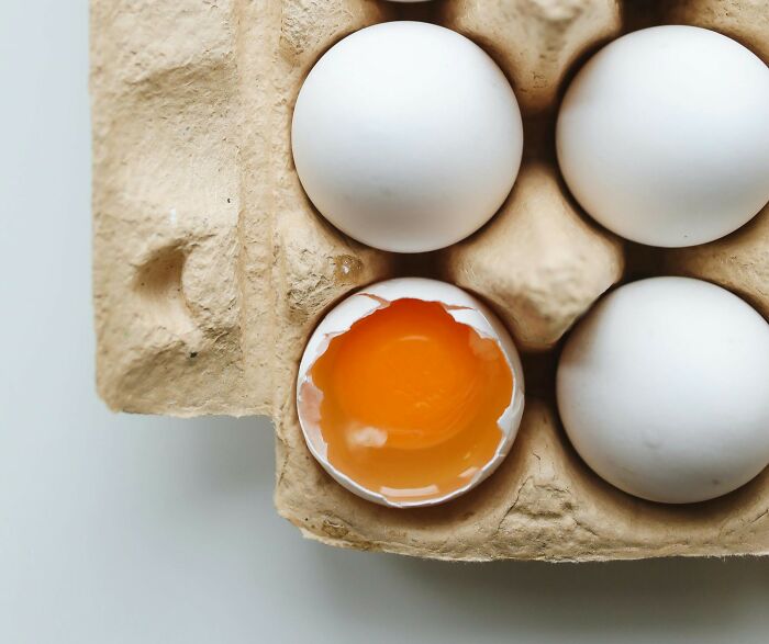 Carton of white eggs with one c*****d open showing yolk, illustrating wild cooking opinions from the internet.