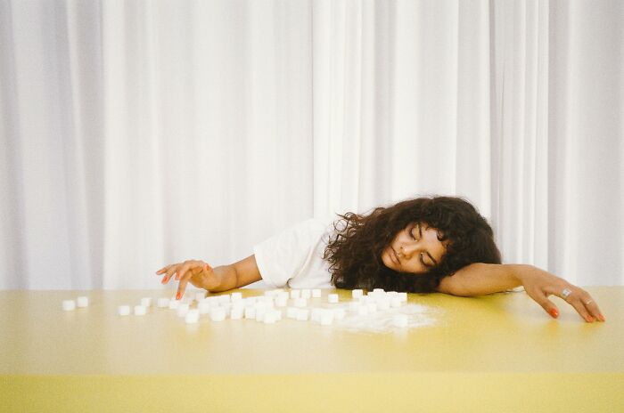 Young woman resting head on a table with scattered sugar cubes, illustrating examples of placebo effect in real life.