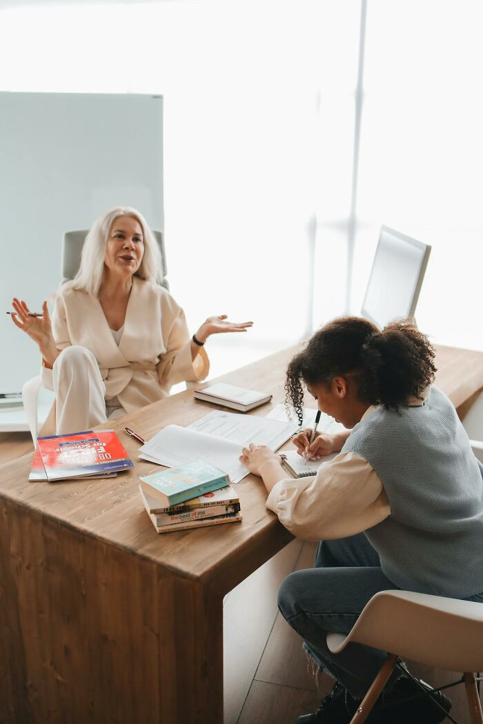 Teacher and student in a bright office, teacher explaining while student takes notes, illustrating unhinged but effective teaching.