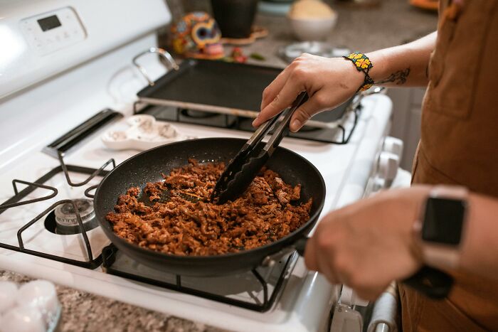 Person cooking ground meat in a pan on stove illustrating food prices comparison in the 1980s and now.