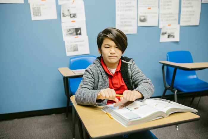Student sitting at a desk in a classroom with open book, illustrating themes of wildest life blunders and personal secrets.