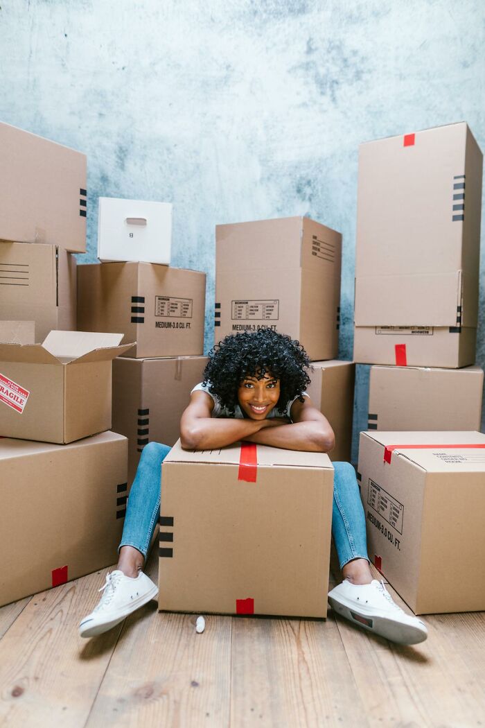 Young woman smiling and sitting among cardboard boxes, representing improved quality of life through positive change.
