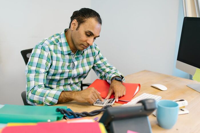 Man in a checkered shirt using a calculator at a desk, illustrating company secret sharing after leaving a job.