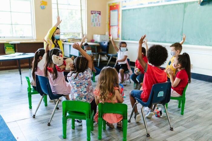 Teacher engaging a diverse group of students wearing masks in a classroom discussion, demonstrating unhinged but effective methods.