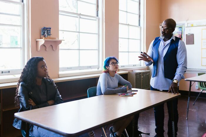 Teacher explaining body changes indicating aging to two attentive students in a bright classroom setting.