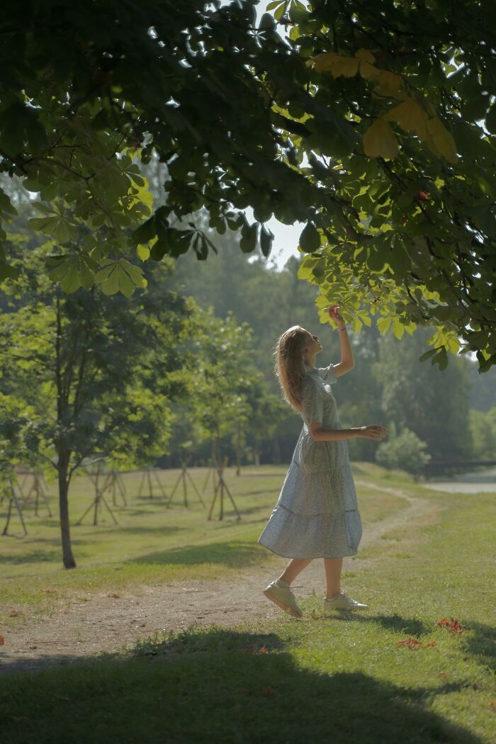 Young woman in a summer dress reaching for leaves in a park, reflecting on middle class challenges for Gen Zers.