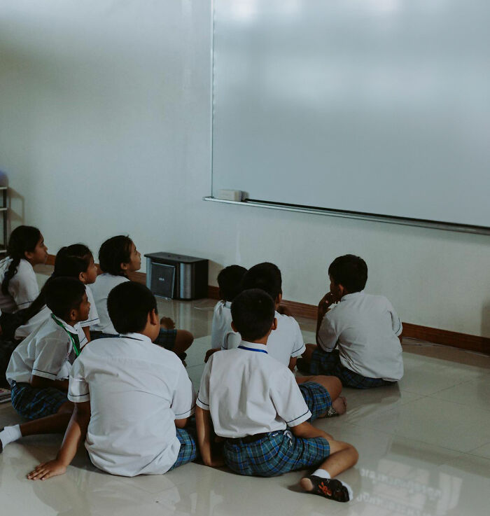 Group of students sitting on the floor in front of a whiteboard, illustrating unhinged teacher methods that actually work.