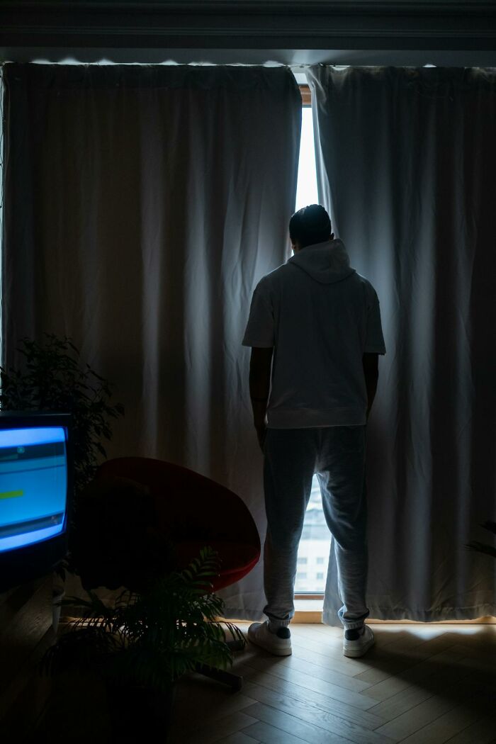 Person standing by curtains with light shining through a window, reflecting on factors that improved quality of life.
