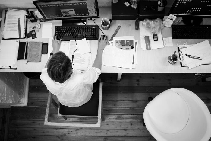 Woman working at a cluttered desk, surrounded by papers and a computer, illustrating microfeminisms supporting women.