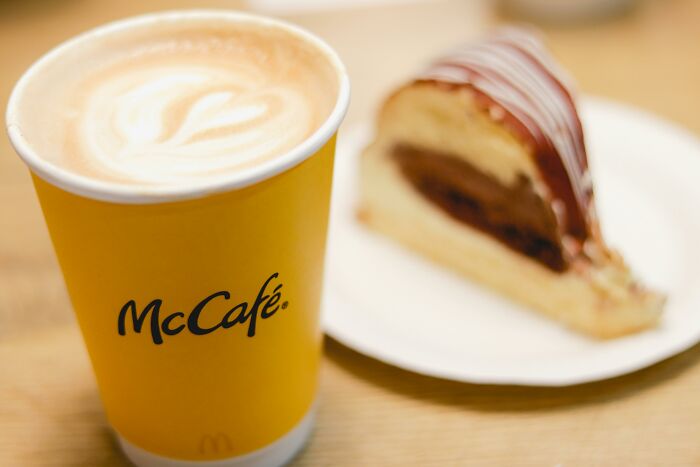 A McCafe coffee cup with latte art next to a slice of chocolate and vanilla cake, highlighting appalling facts people unaware.