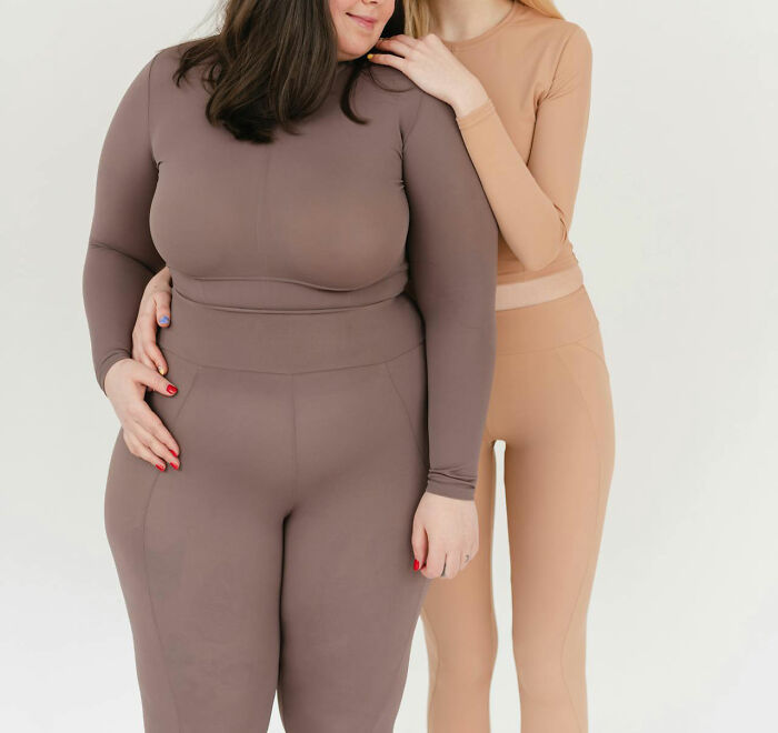 Two women in form-fitting neutral-colored activewear posing closely together, representing questions women would ask men.