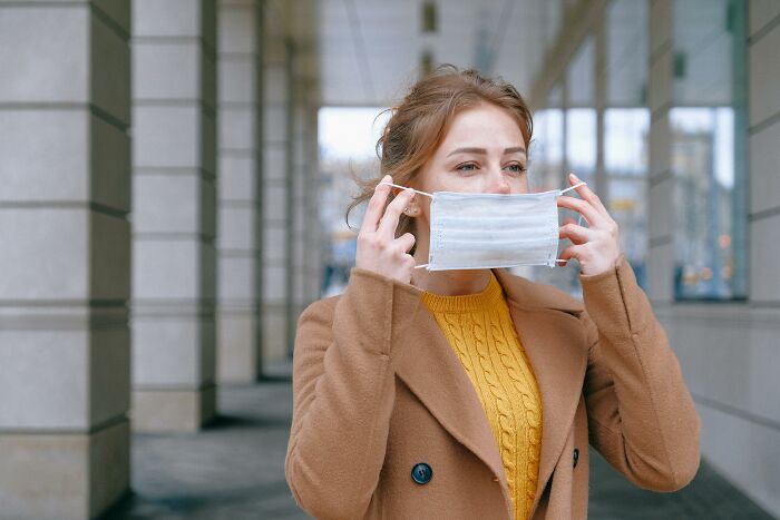 Young woman in a brown coat removing mask outdoors, representing employees sharing strange and dumb things heard from recruiters