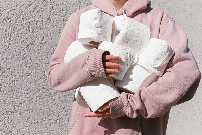 Person wearing a pink hoodie holding multiple rolls of toilet paper illustrating national stereotypes humorously