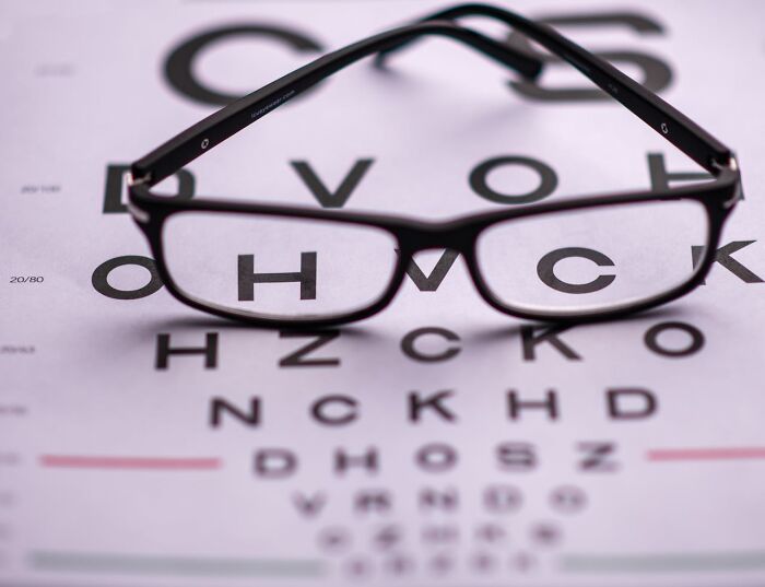 Black eyeglasses resting on an eye chart, illustrating the impact of good or bad genes on vision health.