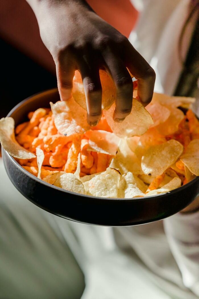 Hand picking potato chips from a bowl of mixed restaurant food snacks in warm lighting.