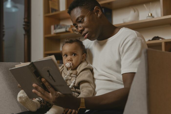 Man reading a book to a baby, illustrating support for women through nurturing and family bonding with microfeminisms.